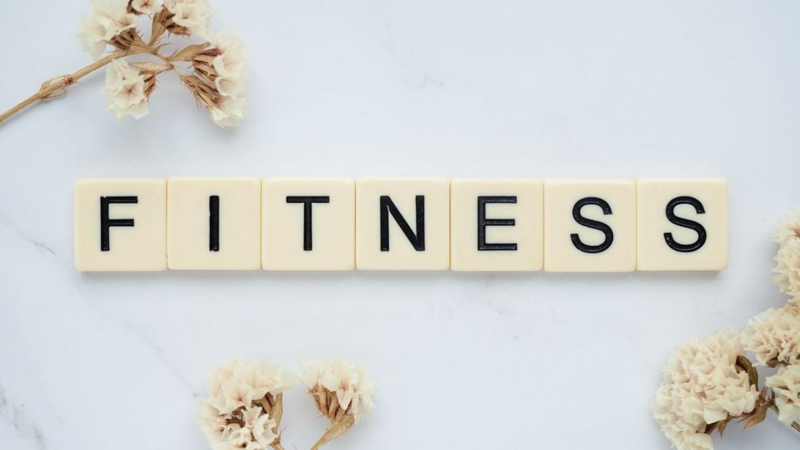 Close-up of scrabble tiles spelling 'FITNESS' on a marble surface with white flowers.
